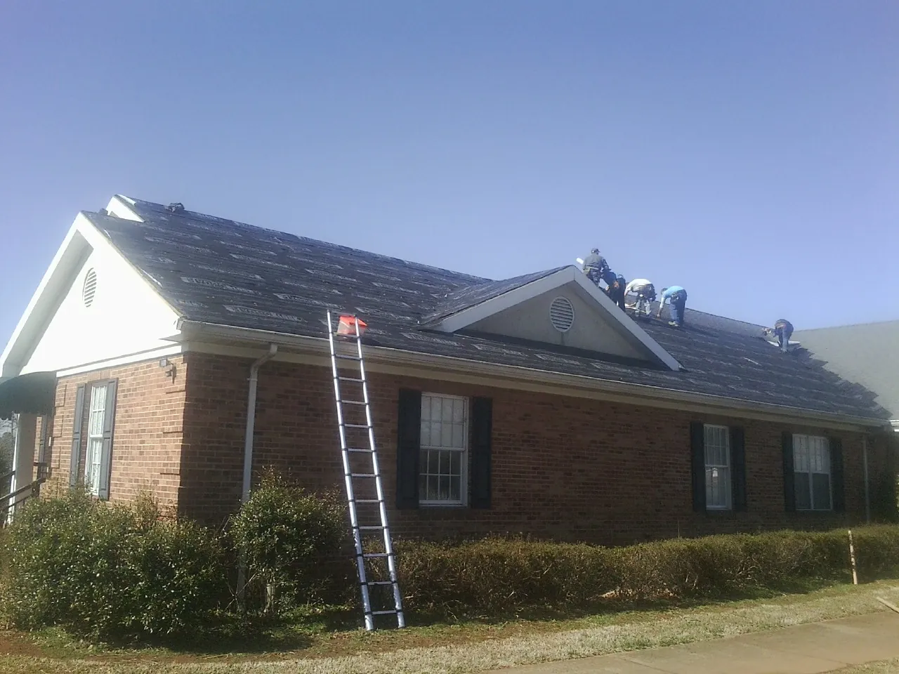 Crew tearing shingles off a brick ranch roof with a ladder set — Metal Roof Repair work by our crew in Englewood
